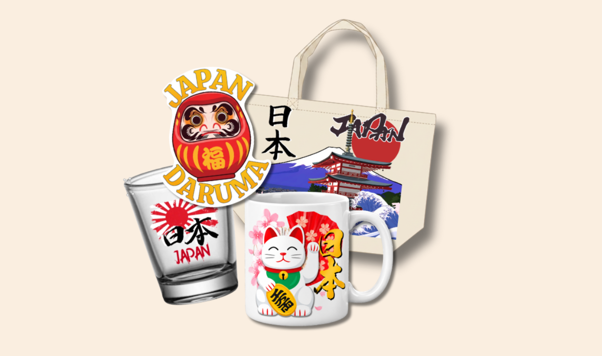 Four Japan souvenirs on beige: a daruma sticker, a tote with pagoda, Mt. Fuji and wave print, a rising-sun shot glass, and a maneki-neko mug with a coin.